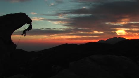 mediumshot of a rockclimber silhouetted by the settingsun hanging from an rock overhang