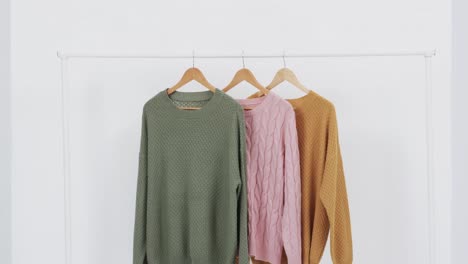 Video-of-three-multi-coloured-sweaters-on-hangers-and-copy-space-on-white-background