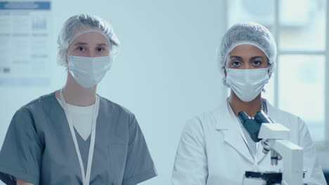 portrait of two female scientists in protective uniform with microscope in lab