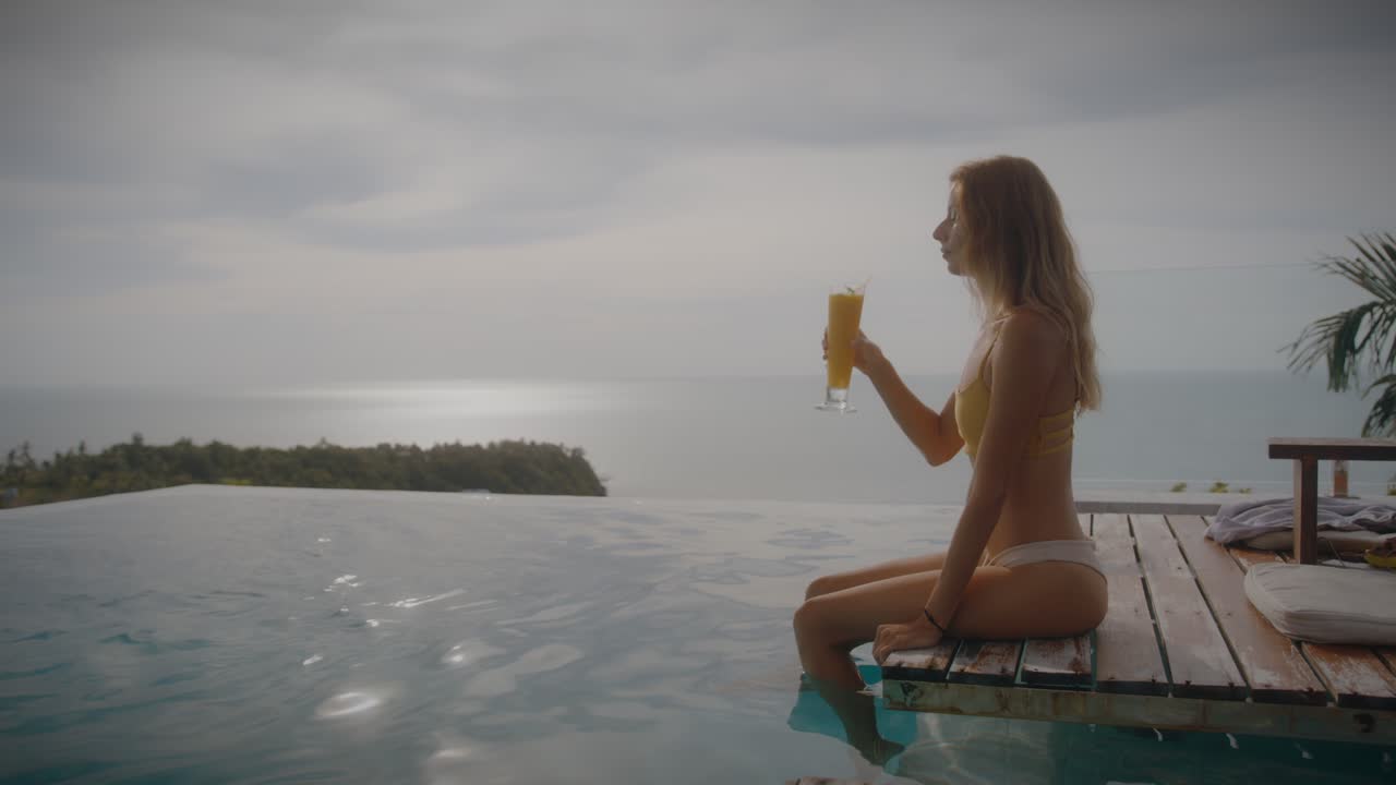 Woman enjoying a cocktail by the pool with ocean view