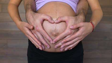 expecting parents form a heart with hands on pregnant woman belly, close up