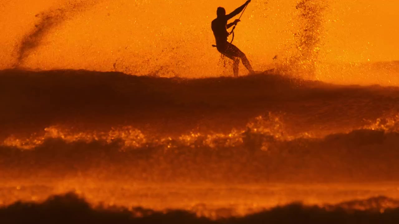 Kiteboarder crash through wave at sunset with sea spray flying everywhere, slomo