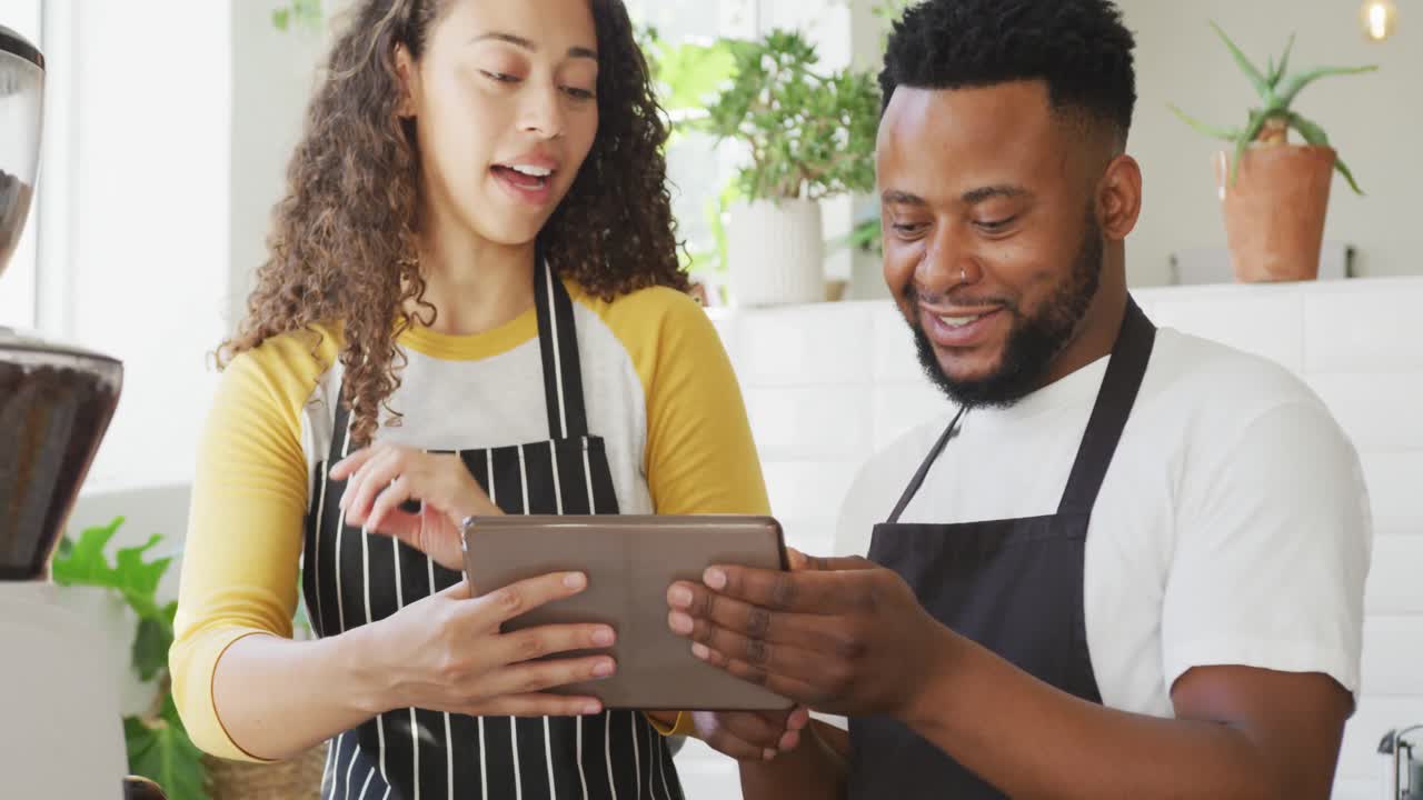 feliz dueño de un café afroamericano y barista biracial usando una tableta en el café
