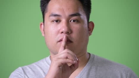 young handsome overweight asian man against green background