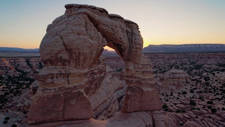 Video aereo che cattura un maestoso arco di arenaria al tramonto, mostrando la sua bellezza naturale da una posizione elevata