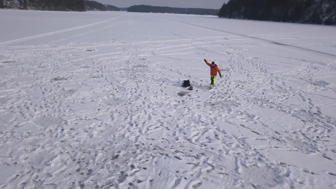Zoom out footage of young man walking from one hole to another with his bait and tackle hoping to be more successful in the new hole.