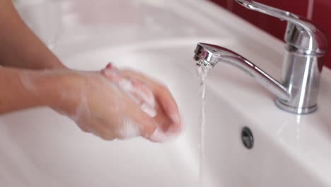 young woman in a red robe washes her hands under running water in a modern bathroom with a round illuminated mirror. high quality 4k footage