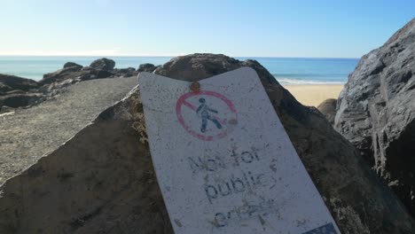 placa de metal de signo grunge atornillada en roca - cielo azul sobre el océano - rocas con señal de no acceso público - tiro estático