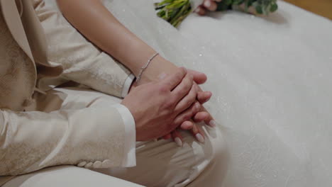 Bride-and-groom-holding-hands-closely,-sitting-together-in-elegant-wedding-attire,-symbolizing-love