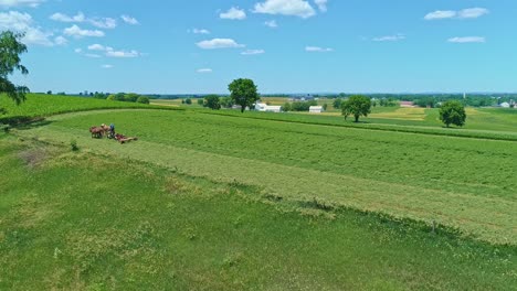 an aerial view of an amish farmer with three horses harvesting his crops looking over the countryside on a beautiful day