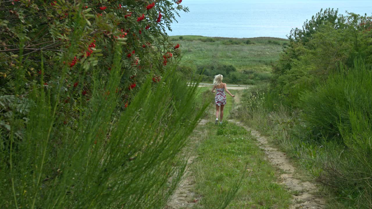 행복과 감사의 표현으로 산책로를 통해 정원 공원에서 달리는 다른 색의 짧은 드레스를 입은 여성