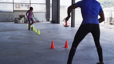 Afroamerikanische-Frau-Macht-Slalom-Mit-Einem-Fußball-In-Einem-Städtischen-Gebäude,-Während-Ein-Mann-Sie-Anfeuert