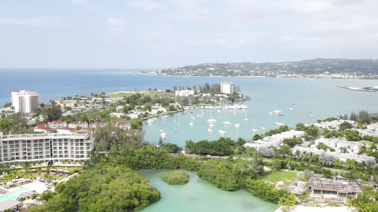 aerial flyover of Freeport community in Montego Bay, Jamaica. The drone glides over the tranquil bay, revealing a prestigious yacht club, and the vibrant blue waters of the Caribbean
