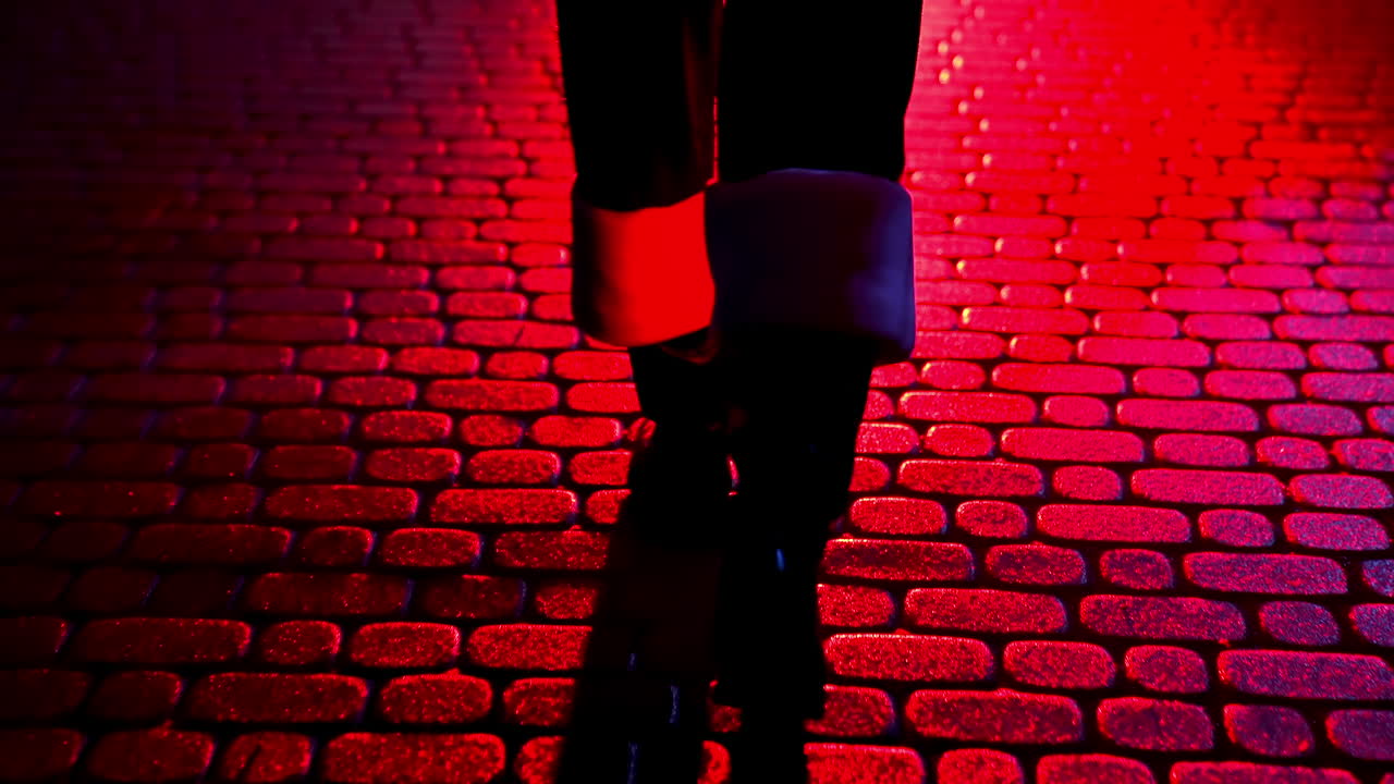Santa Claus walk on pavement. Legs of Father Frost at Christmas outdoors. Boots of Santa walking on a pavement at dark. Red lighting. Back view.