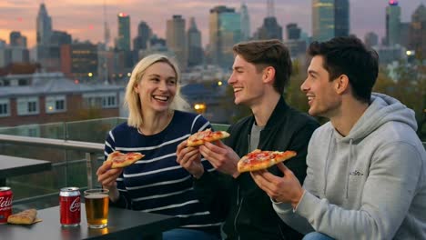 happy friends enjoying pizza and drinks on city rooftop