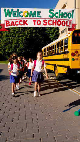 schoolchildren walking past a school bus under a 'welcome back to school' banner