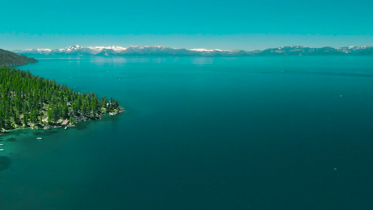 Vista aerea di un sereno lago di montagna con riva boscosa e montagne innevate