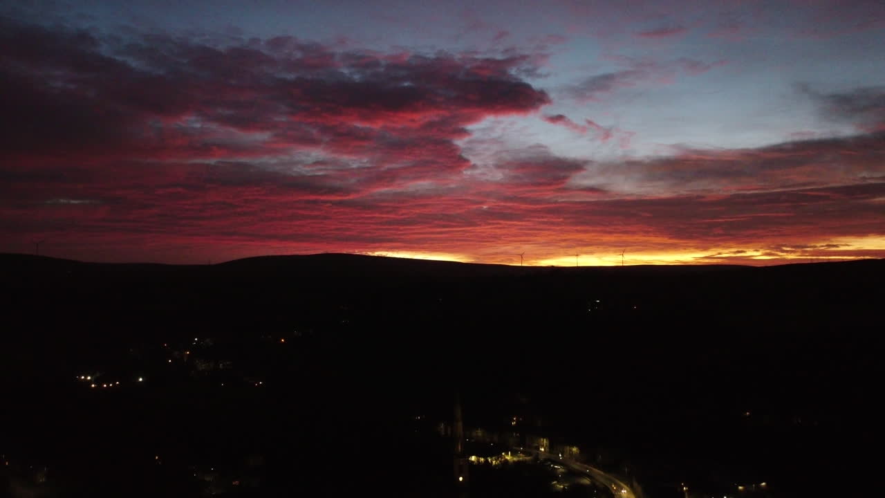 Langsamer, goldener Sonnenuntergang, gefilmt hoch über den abendlichen Straßen von Todmorden in den Hügeln von West Yorkshire, intensive Rot- und Orangetöne strahlen über dem dunklen Horizont.