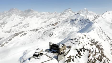 Sobrevuelo-Aéreo-Con-Una-Rotación-Completa-Alrededor-Del-Invierno-Gornergrat-Con-Vistas-Al-Matterhorn,-La-Estación-De-Tren-Y-El-Hotel-Gornergrat,-El-Glaciar-Gorner,-El-Monte-Rosa