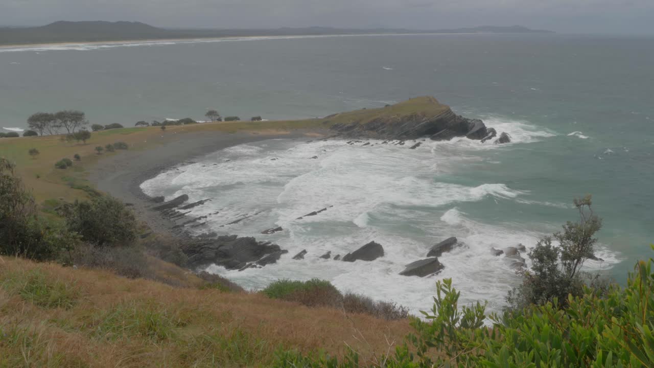 Ondate che colpiscono le rocce costiere a Pebbly Beach e alla penisola di Little Nobby in una giornata grigia - Crescent Head, NSW, Australia.