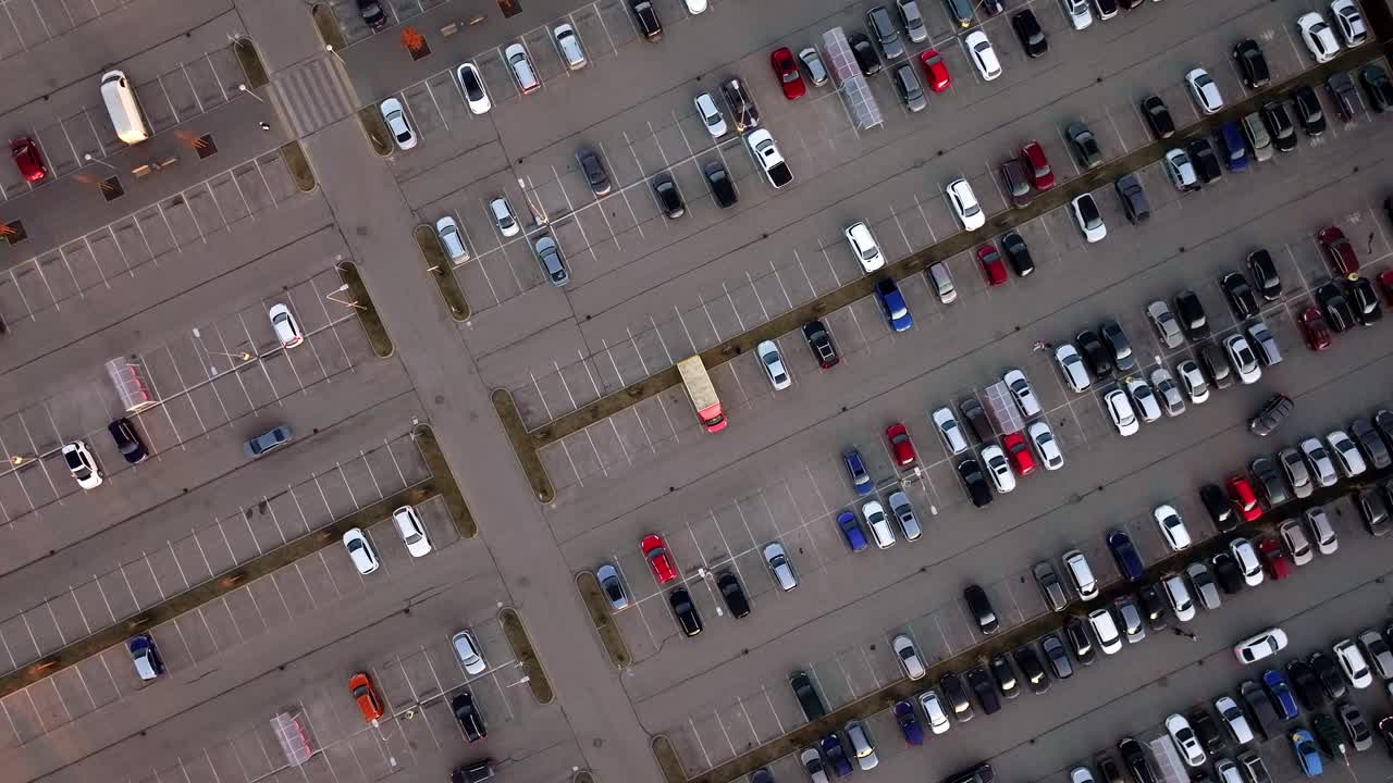 Drone rotates downward above organized city parking lot filled with parked vehicles