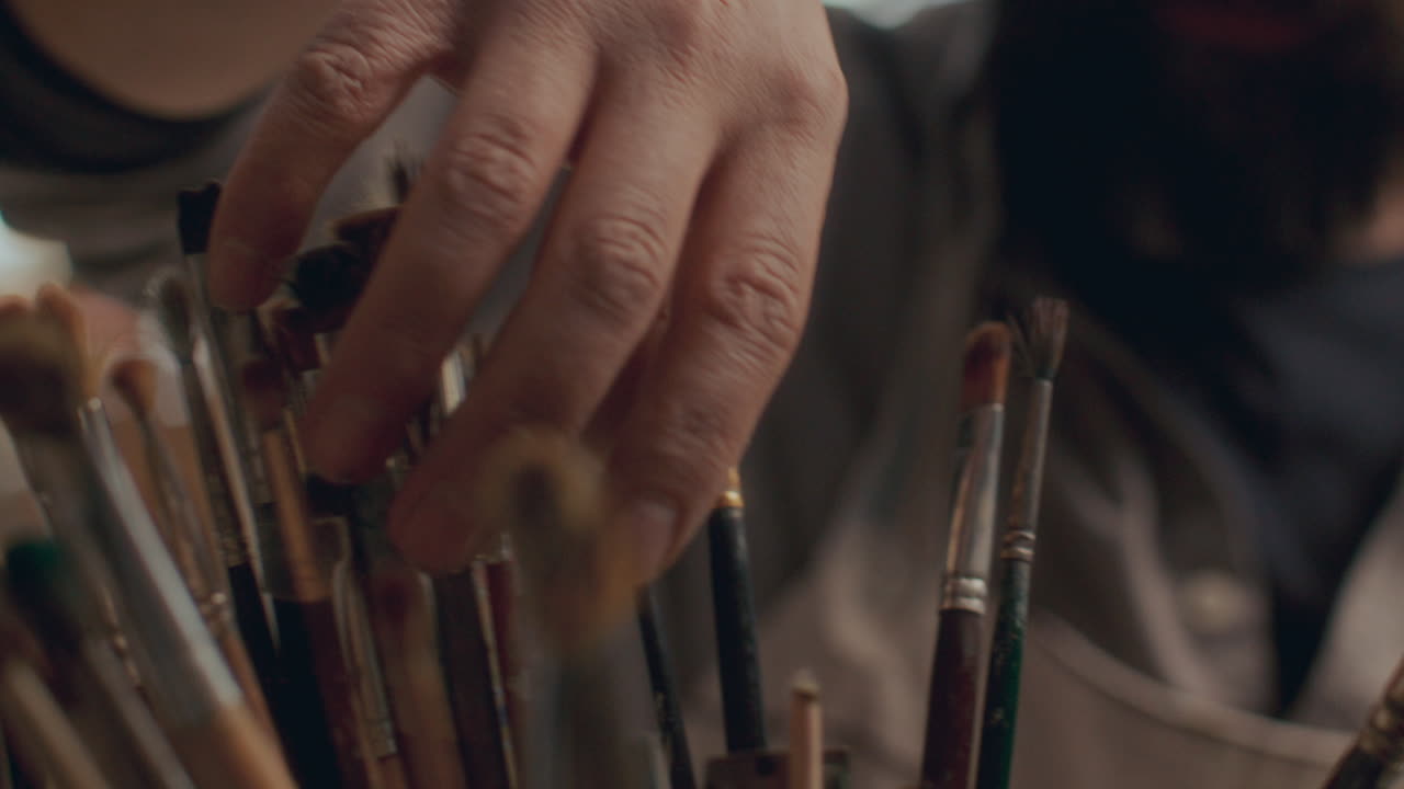 Close Up of Painter Selecting Brushes from Holder in Art Studio