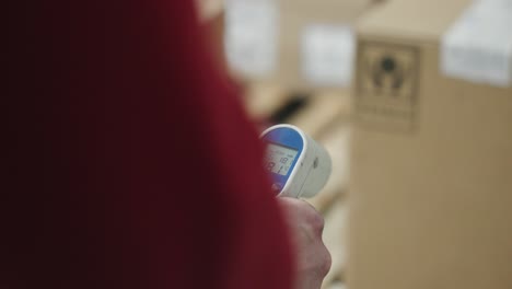 Over-the-shoulder-of-medical-thermometer-gun-with-defocused-boxes-in-background