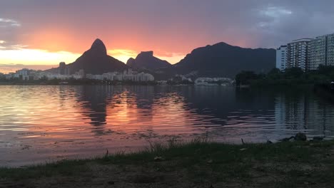 puesta de sol en el lago de la ciudad en río de janeiro detrás de los dos hermanos y la montaña givea con su reflejo en el agua en primer plano
