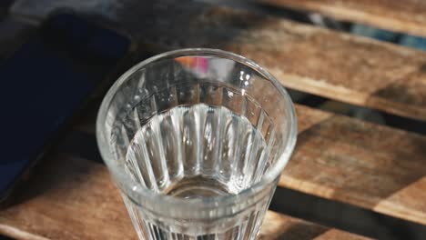 un vaso de agua en una mesa de madera con un teléfono inteligente
