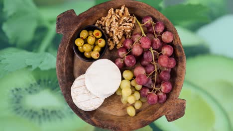 Animación-De-Un-Cuenco-De-Madera-Con-Queso,-Uvas,-Nueces-Y-Aceitunas-Sobre-Vegetales-Verdes