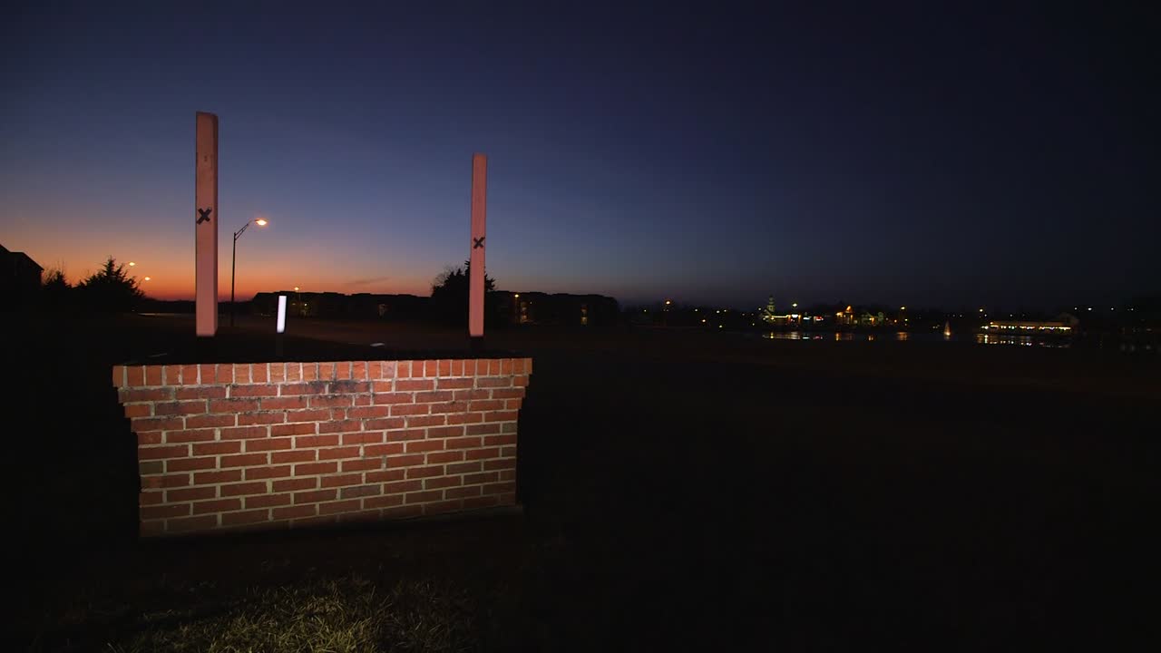 몇 대의 자동차가 일몰 근처의 도로 옆에 있는 밤에 불이 켜진 표지판을 지나 속도를 냅니다.