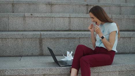 Businesswoman-reading-good-news-on-laptop.-Worker-celebrating-success-in-city