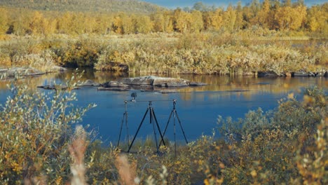 a professional camera on the slider rig stands on the bank of the river surrounded by withered grass and reeds