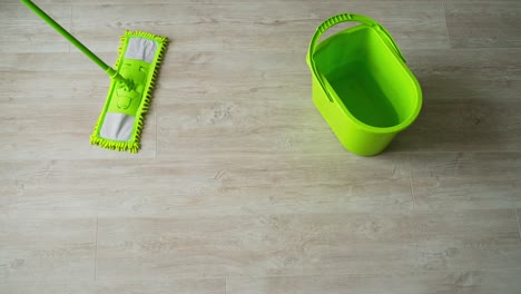 cleaning the parquet floor with a wet mop. green brush and a bucket on wooden floor. housekeeper cleans the floor with a mop. daily chores in apartment. top view.