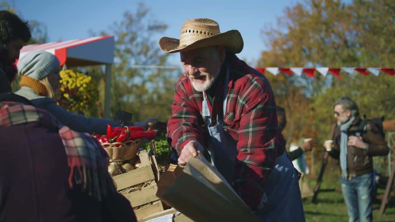 Senior Farmer Selling Fruits and Vegetables Senior Farmer Selling Fruits and Vegetables at the Stall Elderly Woman Puts Products in Paper Eco Bag Local Farmers Market or Autumn Fair Outdoors Agriculture Point of Sale system