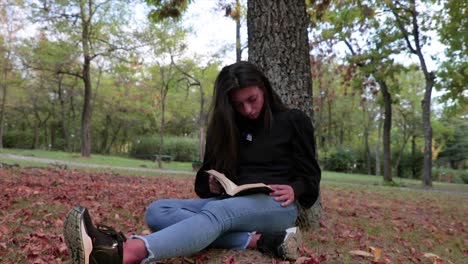 Chica-Leyendo-Un-Libro-En-Un-Parque-Sentado-En-Las-Hojas-De-Otoño-A-Cámara-Lenta