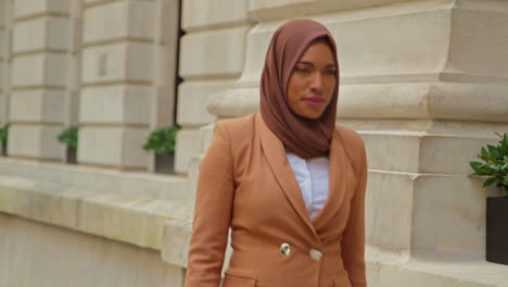 muslim businesswoman wearing hijab with modern business suit walking to work past city office buildings 3