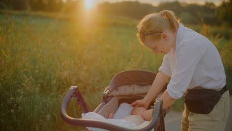 mother gives pacifier to baby in stroller at sunset