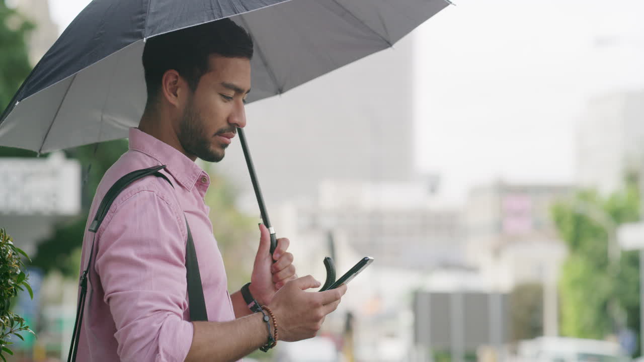 Man using smartphone under umbrella in city