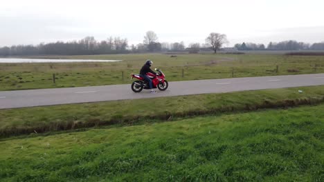 drone shot of motorcyclist standing still in between grass fields