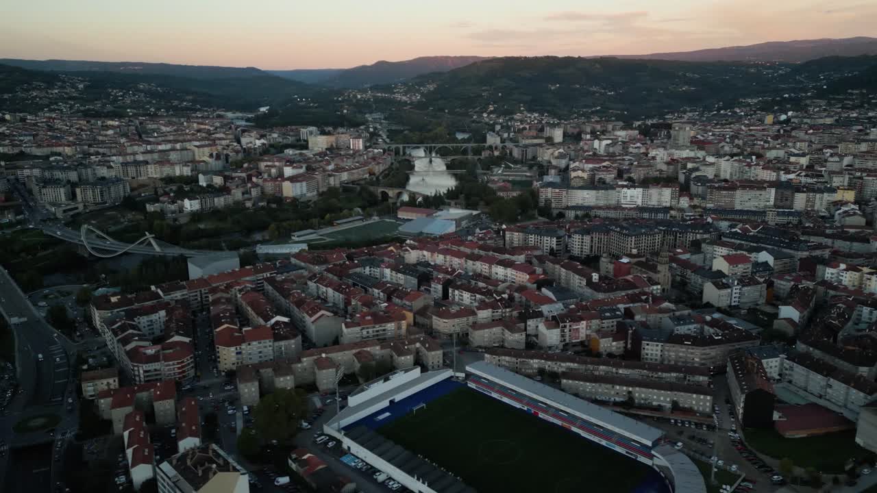 Aerial trucking pan above football stadium in middle of apartment buildings along river in Ourense Spain at dusk sunset