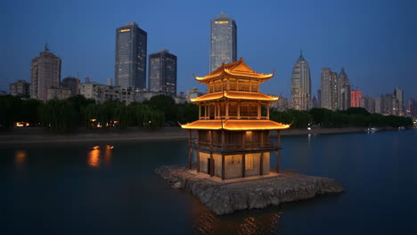 illuminated traditional pavilion on a river at night with city skyline