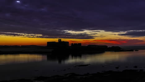 timelapse en una hermosa puesta de sol naranja al borde de un lago con siluetas de edificios en el fondo