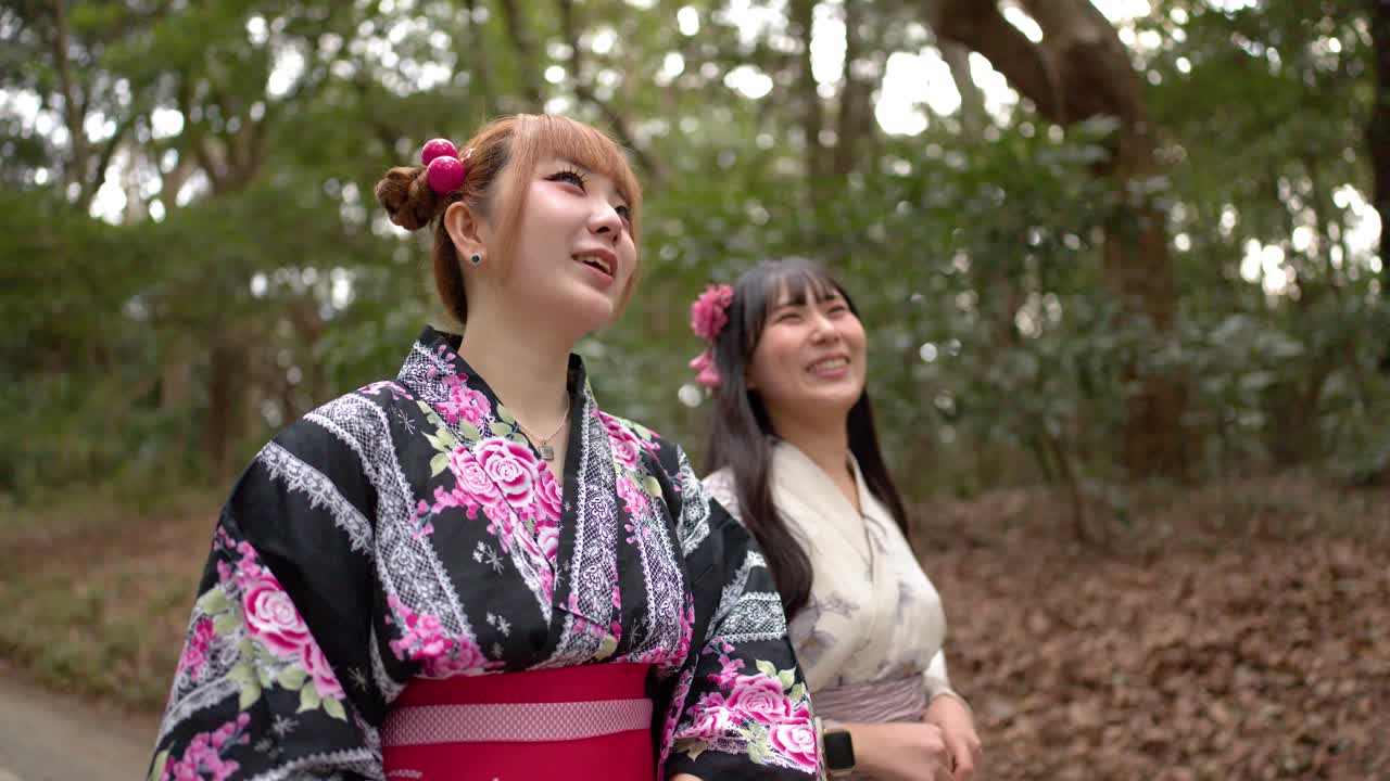 東京の緑豊かな森を、花柄の着物を着た笑顔の日本人女性2人が歩く。