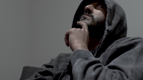 A-close-up-shot-of-an-Indian-Man-wearing-a-hoodie,-head-tilted-back-gazing-up-at-the-roof-lost-in-deep-thoughts-with-his-hand-on-his-chin