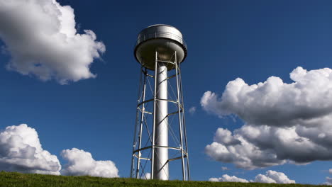 water tower on a grassy hill under a blue sky with clouds