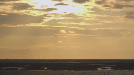 Untergehende-Sonnenstrahlen,-Die-Sich-über-Den-Horizont-Bewegen,-Während-Sich-In-Der-Ferne-Windmühlen-Drehen