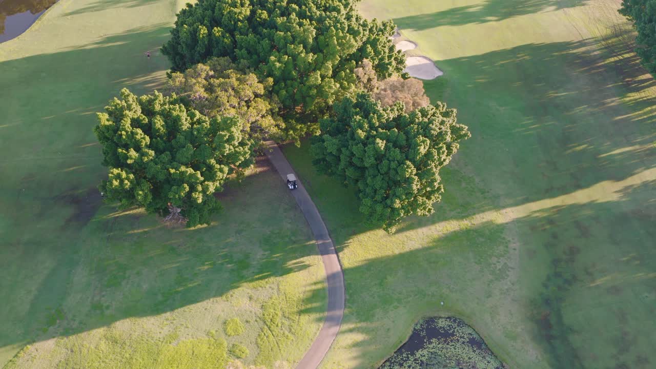 Drone footage captures lush green fairways, trees, and water hazards on a Gold Coast golf course during golden sunset hour