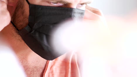 hombre barbudo quita máscaras quirúrgicas dobles de la cara para respirar aire fresco, habitación luminosa
