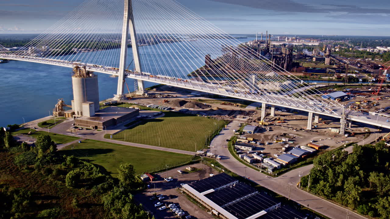 Aerial camera moves over the Gordie Howe Bridge toward riverfront industry